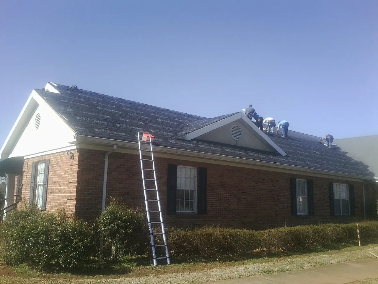 Crew tearing shingles off a brick ranch roof with a ladder set — Metal Roof Repair work by our crew in New Harmony