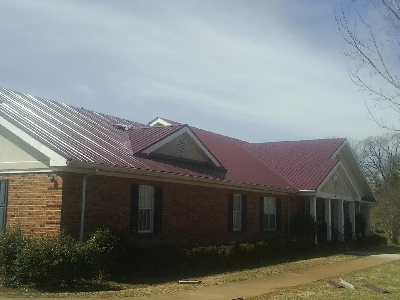 Red metal roof with gabled entries on a long brick building, from a Hail Damage Roof Repair job in New Harmony