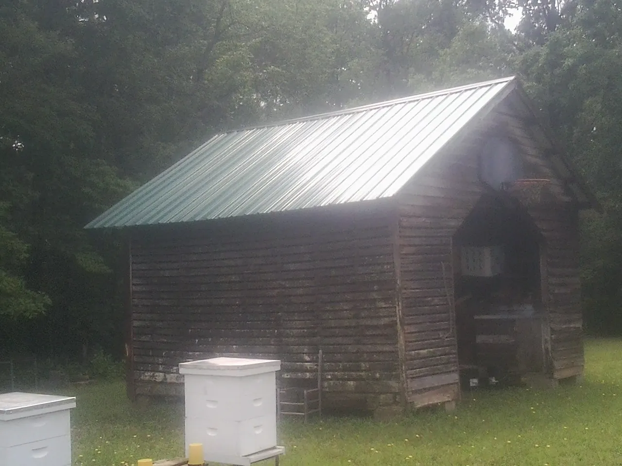 Green metal roof on a weathered barn beside stacked beehives in New Harmony