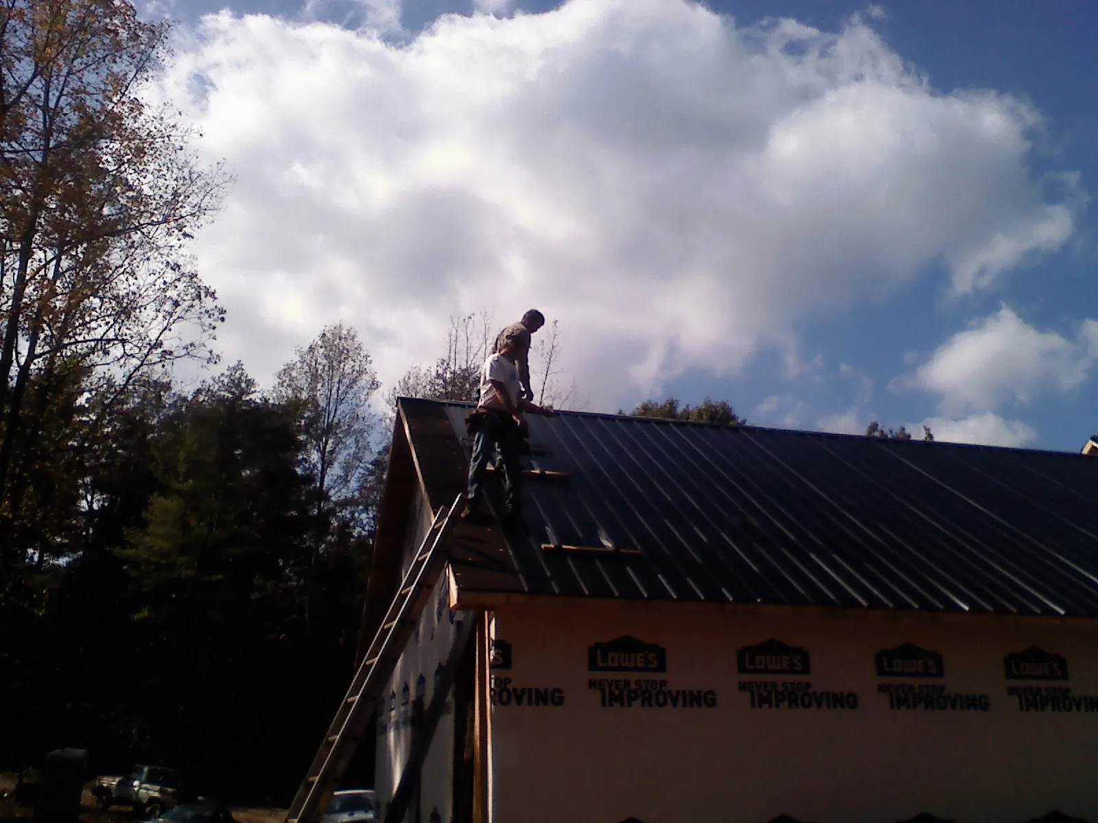 Roofer fastening dark metal panels high against a cloudy sky, from a Roof Inspection job in New Harmony